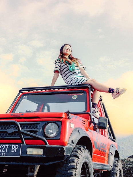 Girl sitting on a red Jeep at Black Lava Exploration, Mt. Batur, Bali.