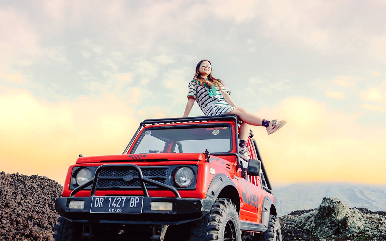 Girl sitting on a red Jeep at Black Lava Exploration, Mt. Batur, Bali.