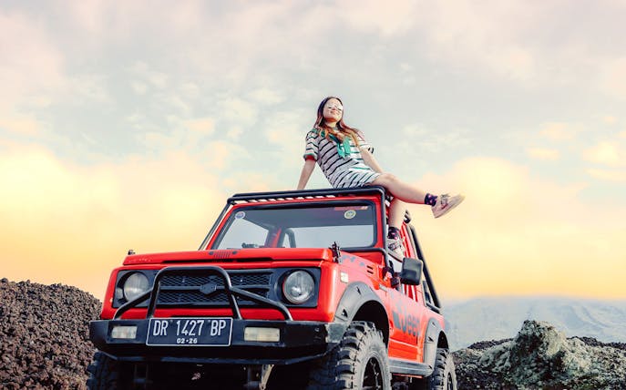 Girl sitting on a red Jeep at Black Lava Exploration, Mt. Batur, Bali.