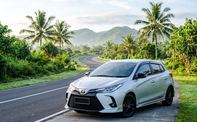 Toyota Yaris parked on a scenic tropical road with palm trees and mountains.