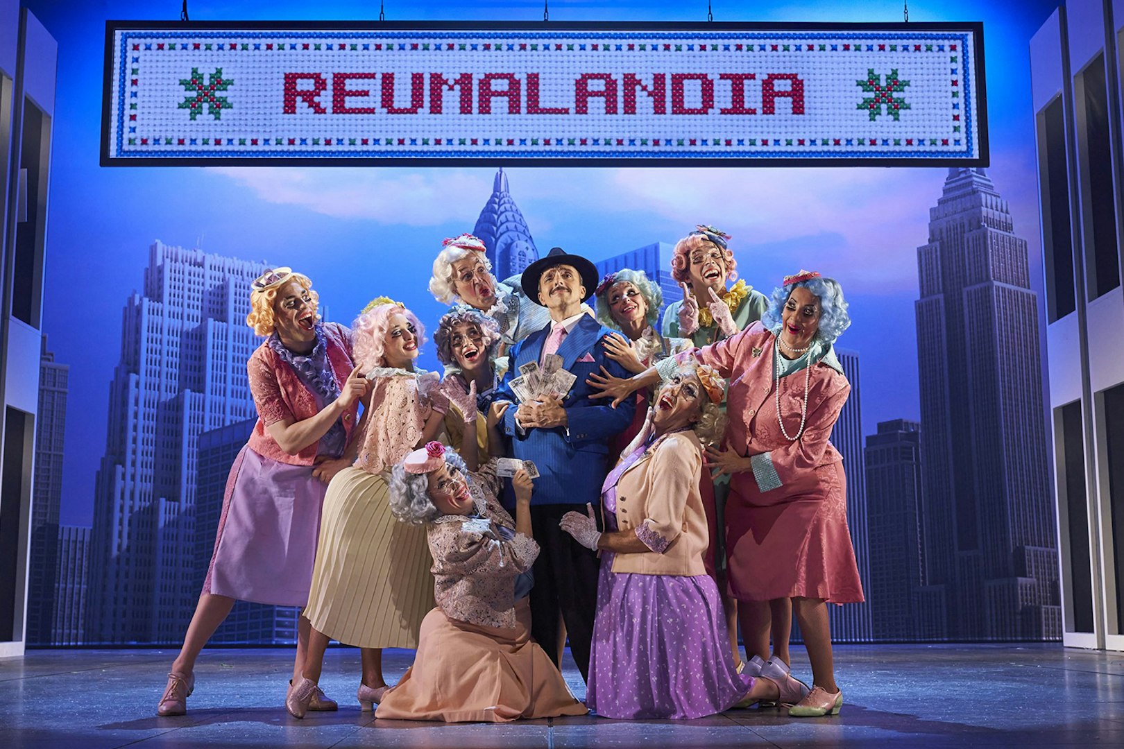 Cast of "The Producers" performing on stage with New York City backdrop.