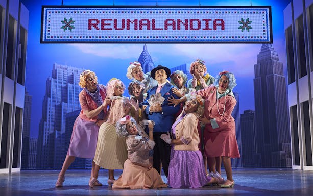 Cast of "The Producers" performing on stage with New York City backdrop.