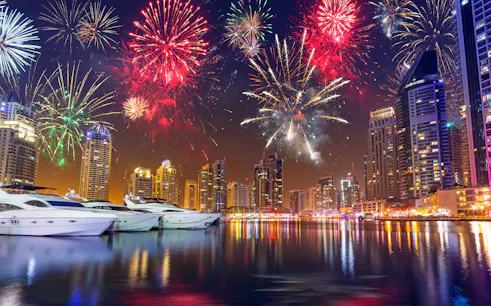 Fireworks over Dubai Marina skyline with yachts on the water, UAE.