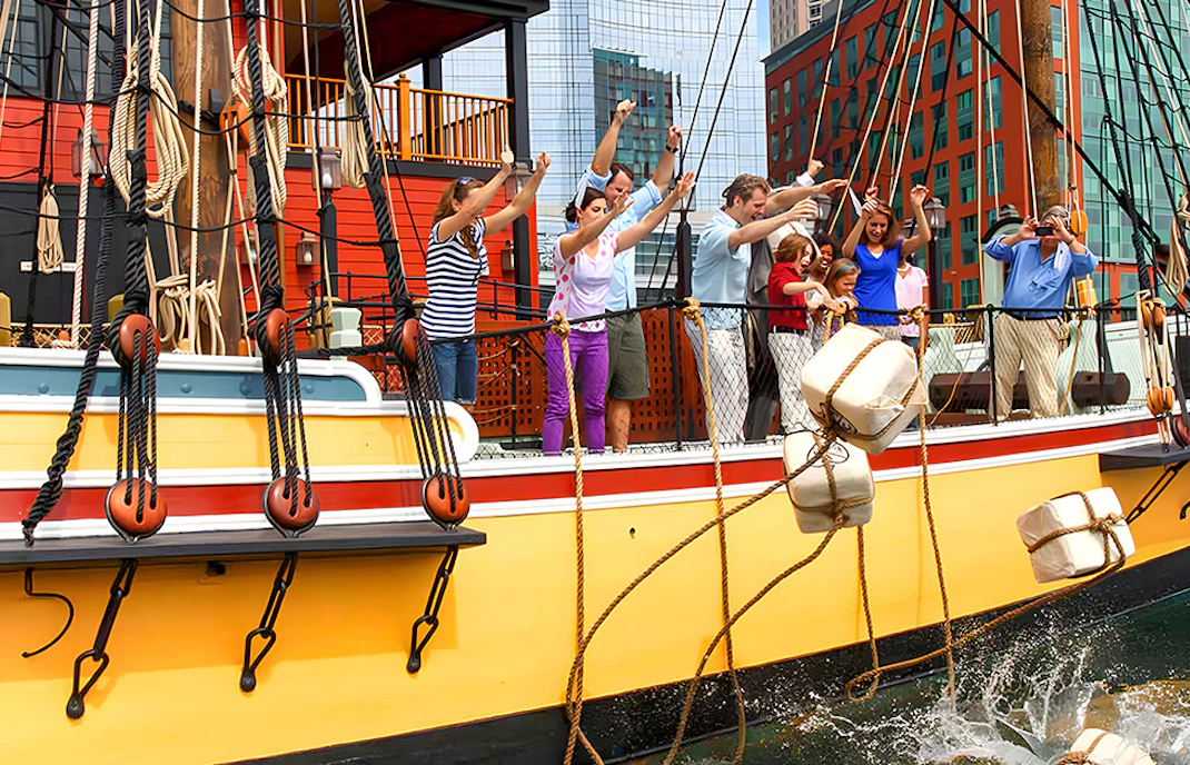 Tourists reenacting Boston Tea Party by throwing tea chests from a ship in Boston Harbor.