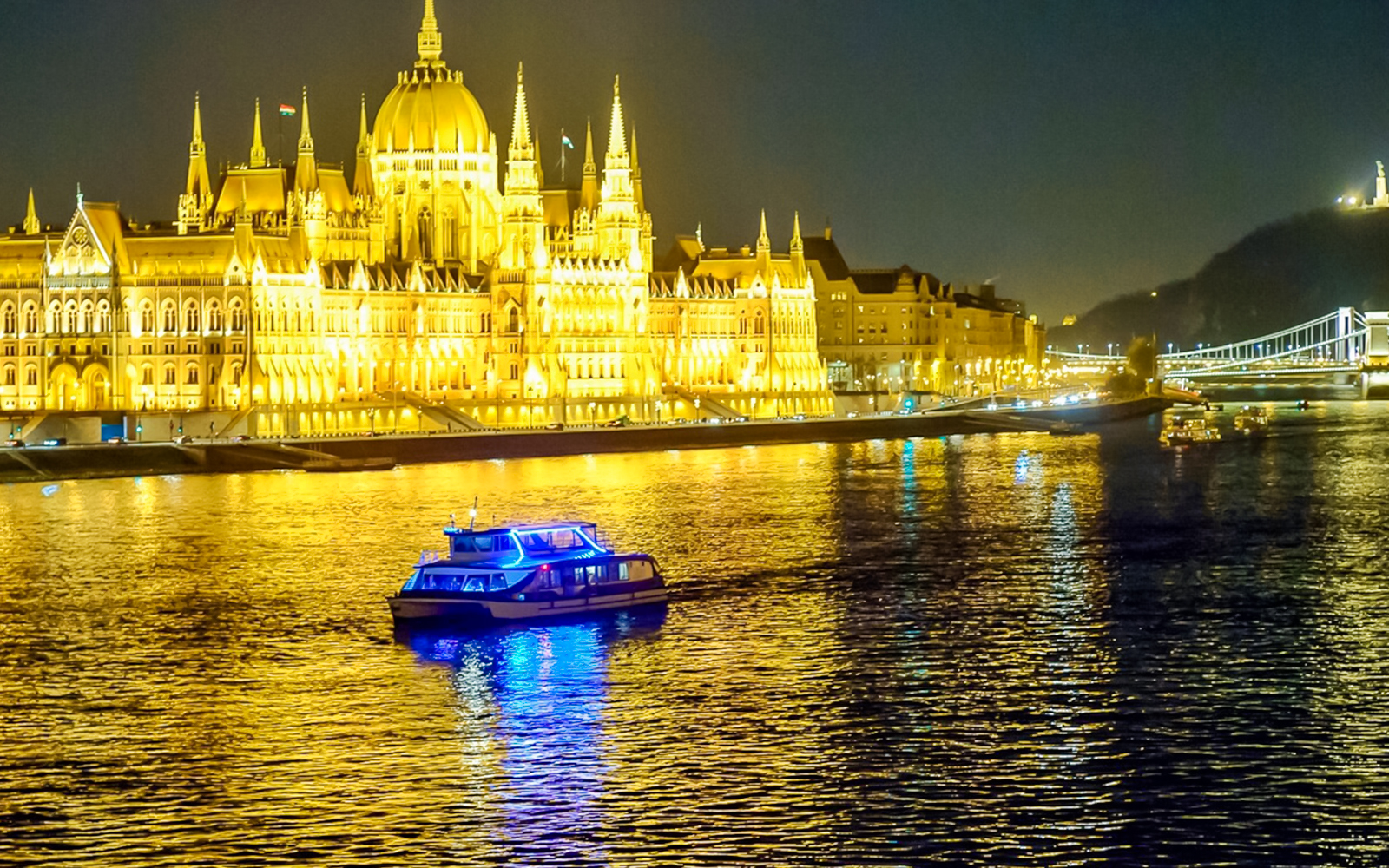 Dinner cruise boat on the Danube River with Budapest Parliament illuminated at night.