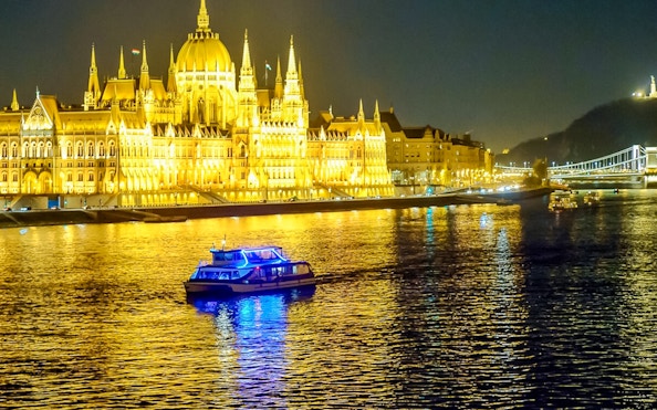 Dinner cruise boat on the Danube River with Budapest Parliament illuminated at night.