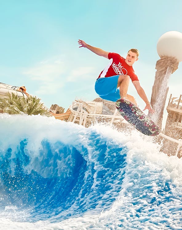 Person surfing on artificial wave at Yas Waterworld, Dubai theme park.