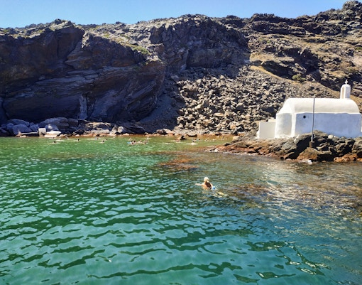 Swimmers near the rocky coast and white chapel of Nea Kameni, Santorini.