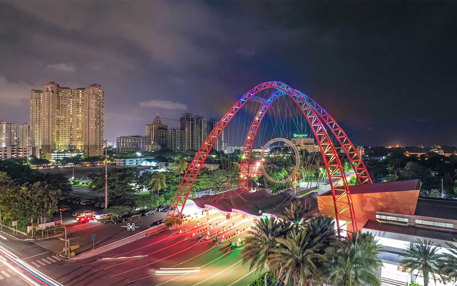 Ancol entrance gate illuminated at night with city skyline in Jakarta, Indonesia.