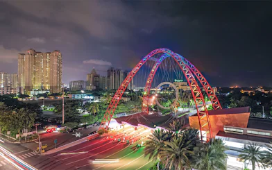 Ancol entrance gate illuminated at night with city skyline in Jakarta, Indonesia.