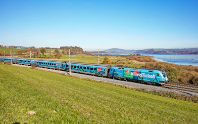 Train traveling through scenic countryside near a lake, promoting KlimaTicket.
