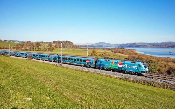 Train traveling through scenic countryside near a lake, promoting KlimaTicket.