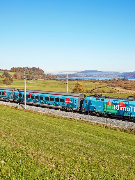 Train traveling through scenic countryside near a lake, promoting KlimaTicket.