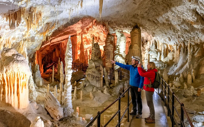 Tour guide with tourist exploring stalactites in Postojna Cave, Slovenia.