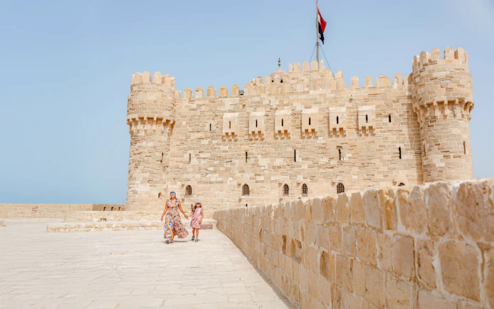 Tourist family exploring Qaitbay Citadel, Alexandria, with historic stone walls and coastal views.