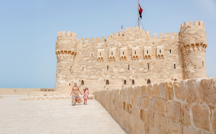 Tourist family exploring Qaitbay Citadel, Alexandria, with historic stone walls and coastal views.