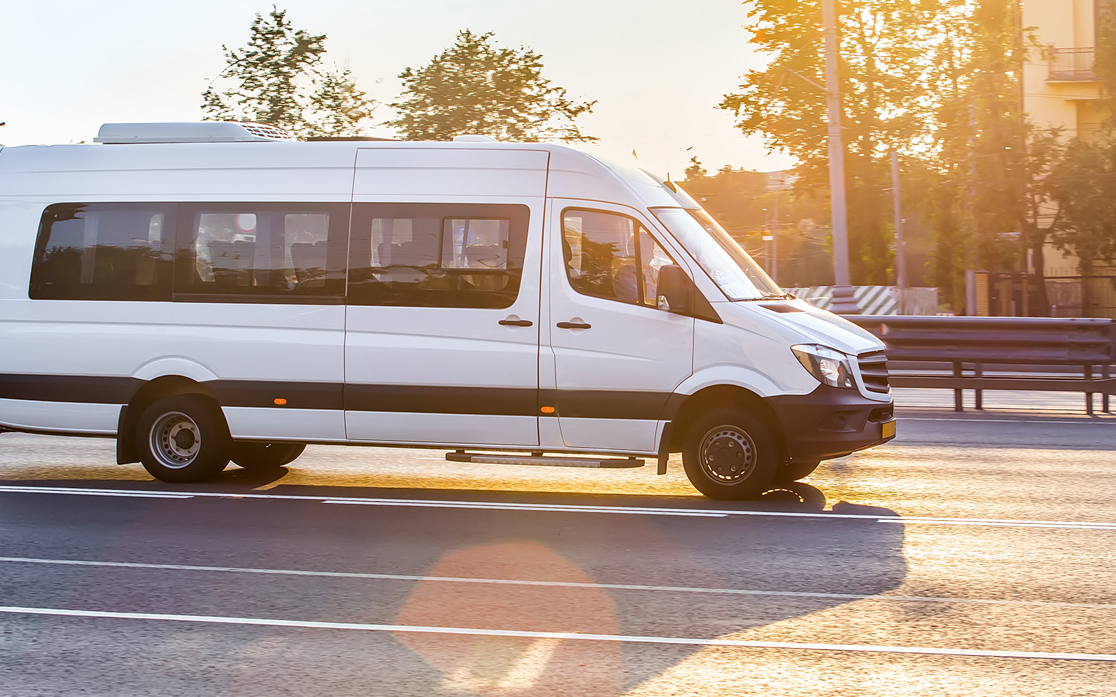 White Mercedes-Benz Sprinter van driving on a sunny road.