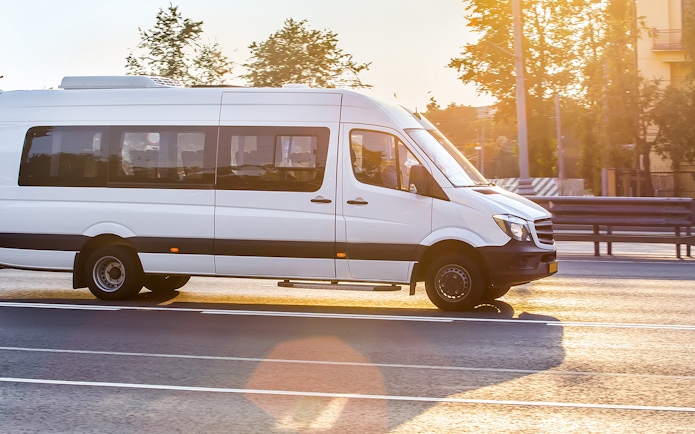 White Mercedes-Benz Sprinter van driving on a sunny road.