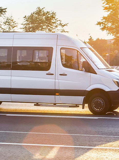 White Mercedes-Benz Sprinter van driving on a sunny road.