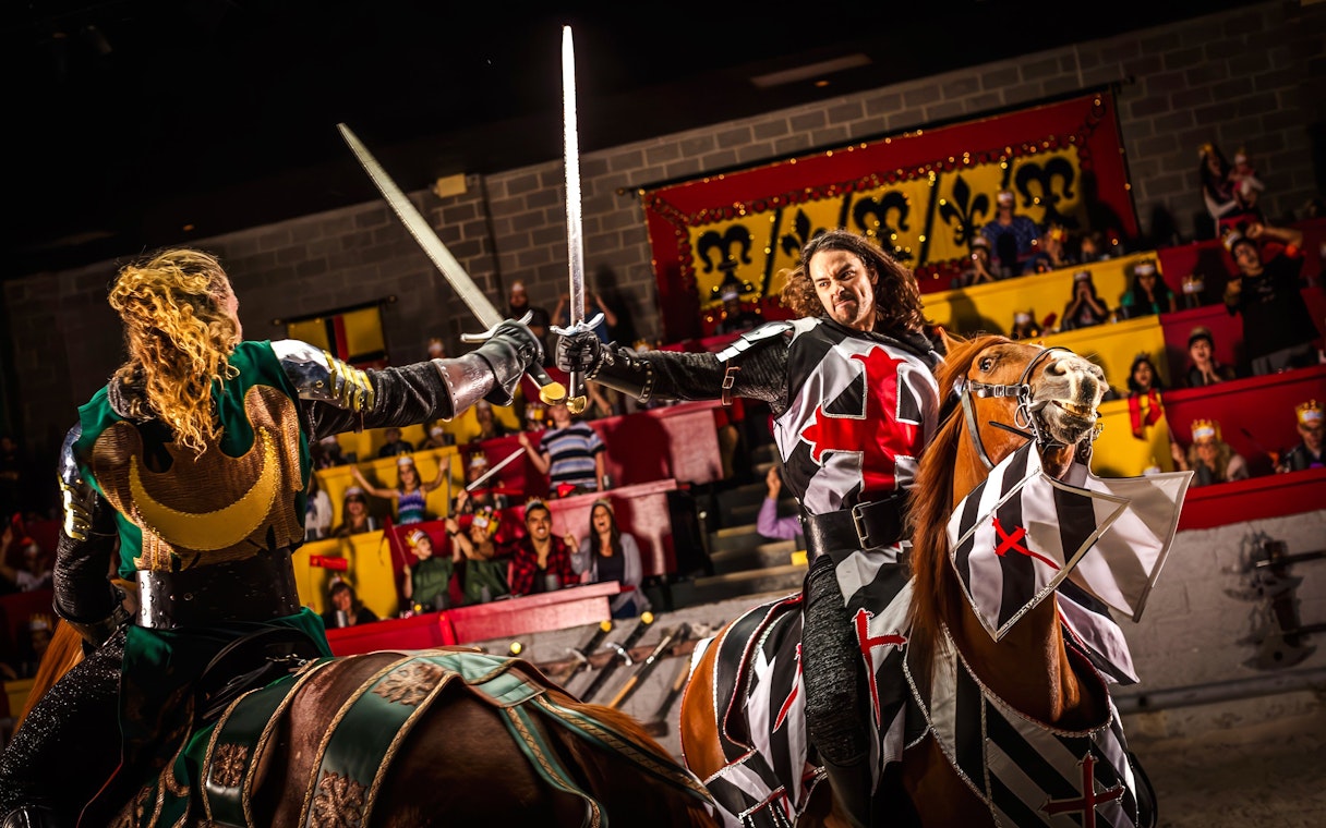 Knights jousting on horseback at Medieval Times Dinner and Show, with an audience watching.