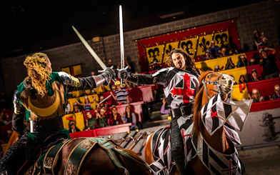Knights jousting on horseback at Medieval Times Dinner and Show, with an audience watching.