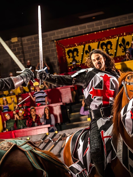 Knights jousting on horseback at Medieval Times Dinner and Show, with an audience watching.