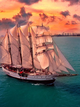 Sailing ship Royal Albatross at sunset near city skyline.