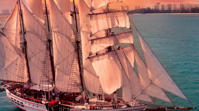 Sailing ship Royal Albatross at sunset near city skyline.