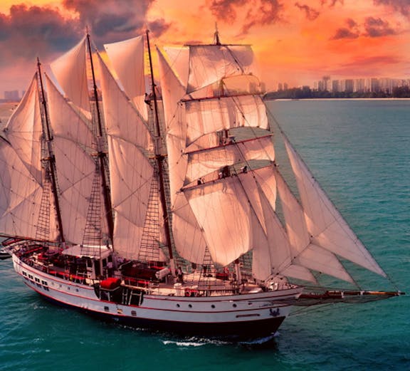 Sailing ship Royal Albatross at sunset near city skyline.