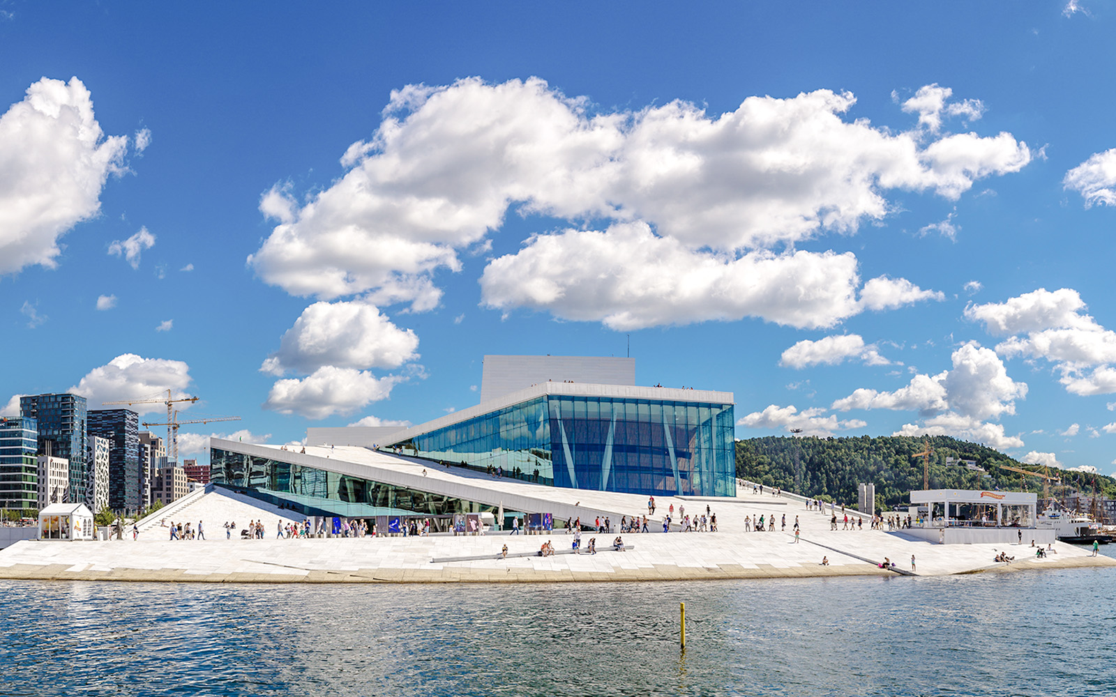 Oslo Opera House with visitors walking on its sloped roof by the waterfront.