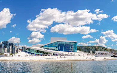 Oslo Opera House with visitors walking on its sloped roof by the waterfront.