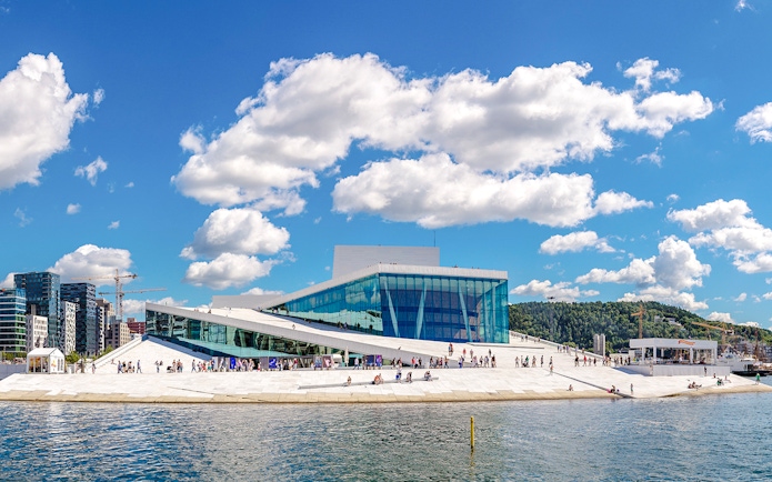 Oslo Opera House with visitors walking on its sloped roof by the waterfront.