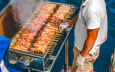 Chef grilling skewers on a catamaran cruise in Santorini.