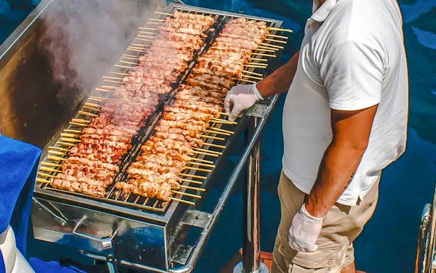 Chef grilling skewers on a catamaran cruise in Santorini.