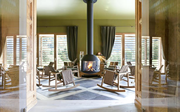 Rocking chairs around a fireplace at QC Terme Chamonix spa with mountain views.
