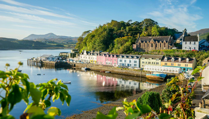 Colorful buildings along the Harbour of Portree, Isle of Skye, with hills in the background.