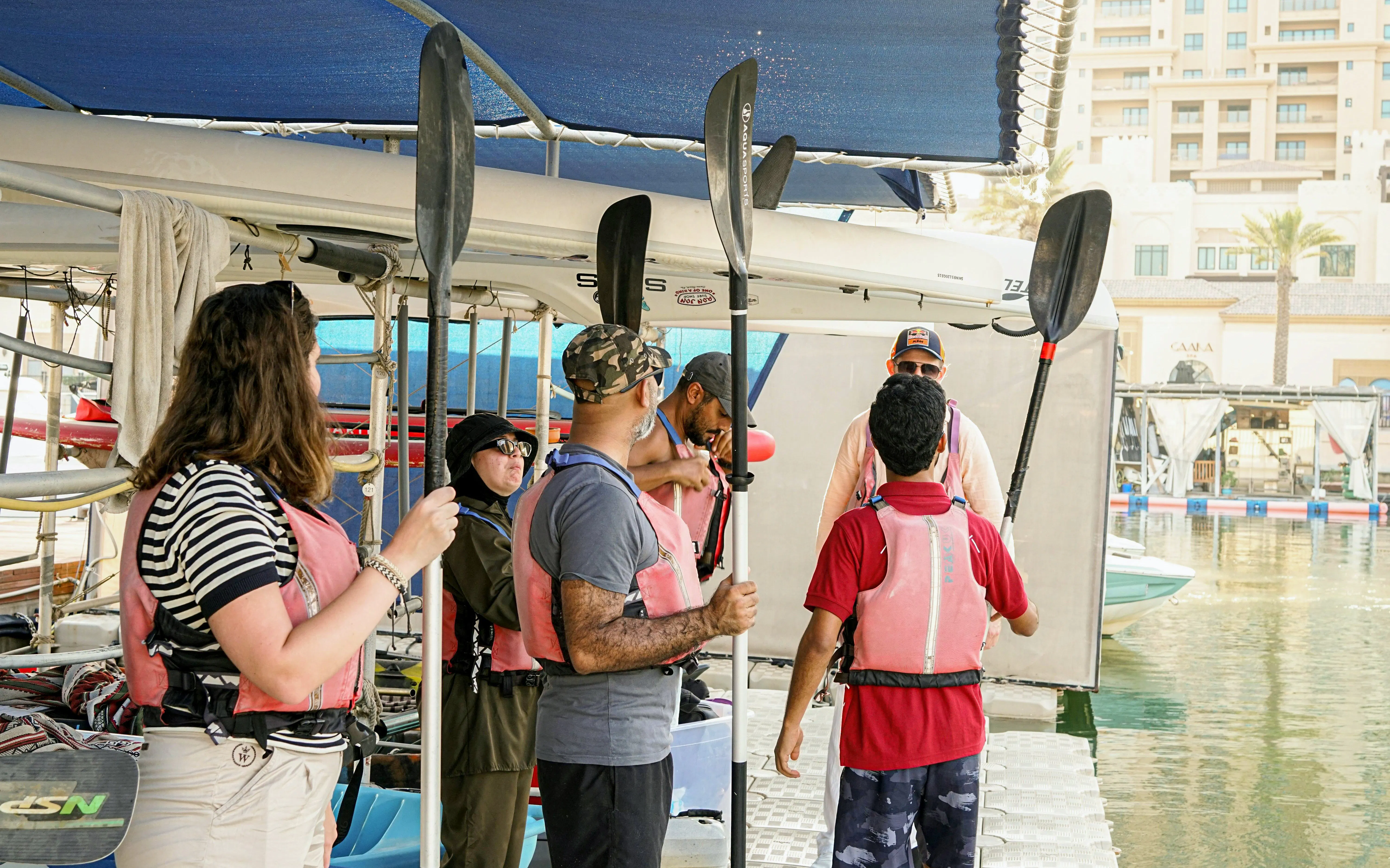 Group preparing for The Pearl Guided Kayak Tour in Doha, holding paddles on a dock.