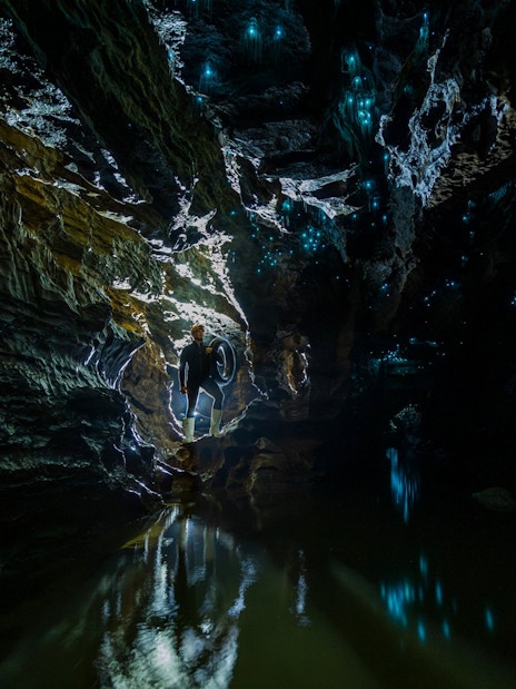 Person exploring Okohua Glowworm Cave with glowing blue lights on cave walls, Waitomo Experience.