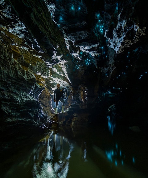 Person exploring Okohua Glowworm Cave with glowing blue lights on cave walls, Waitomo Experience.