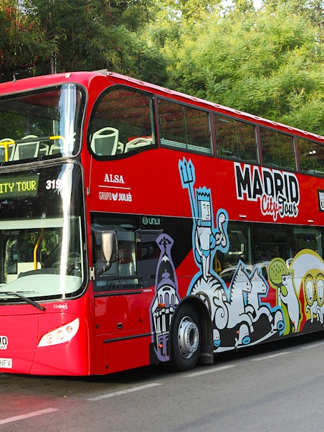 Red double-decker hop-on hop-off bus in Madrid near historic buildings.