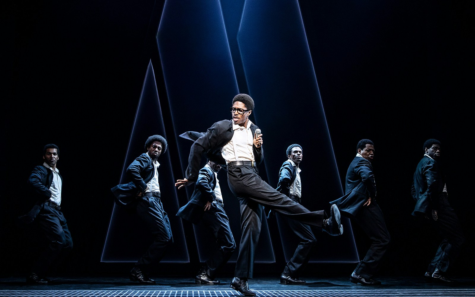Performers dancing energetically on stage in "Ain't Too Proud" musical.