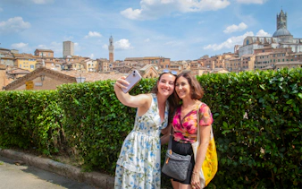 Tourists taking a selfie with Siena skyline in the background, featuring Torre del Mangia, Tuscany.