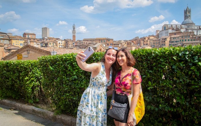 Tourists taking a selfie with Siena skyline in the background, featuring Torre del Mangia, Tuscany.