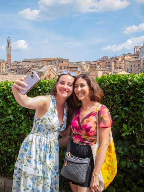Tourists taking a selfie with Siena skyline in the background, featuring Torre del Mangia, Tuscany.