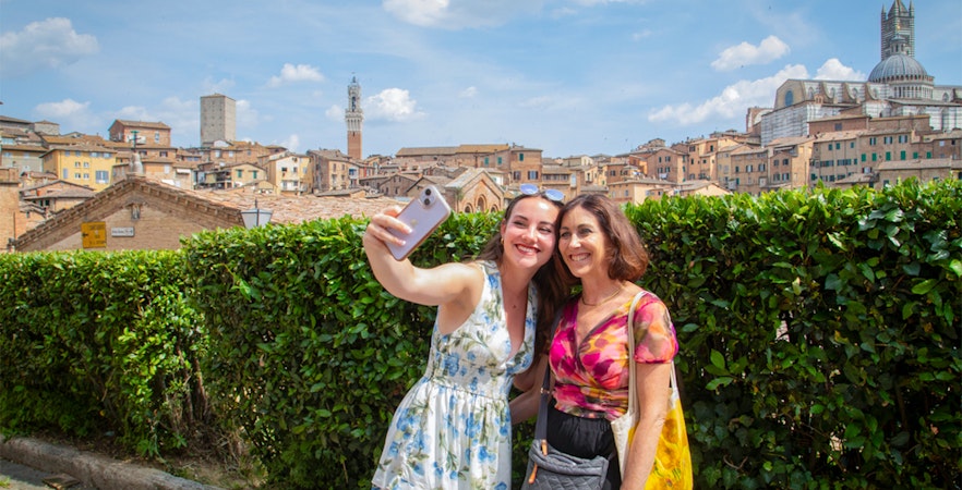 Tourists taking a selfie with Siena skyline in the background, featuring Torre del Mangia, Tuscany.