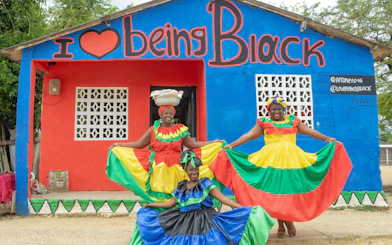 Traditional dancers in colorful dresses pose in front of San Basilio de Palenque mural.