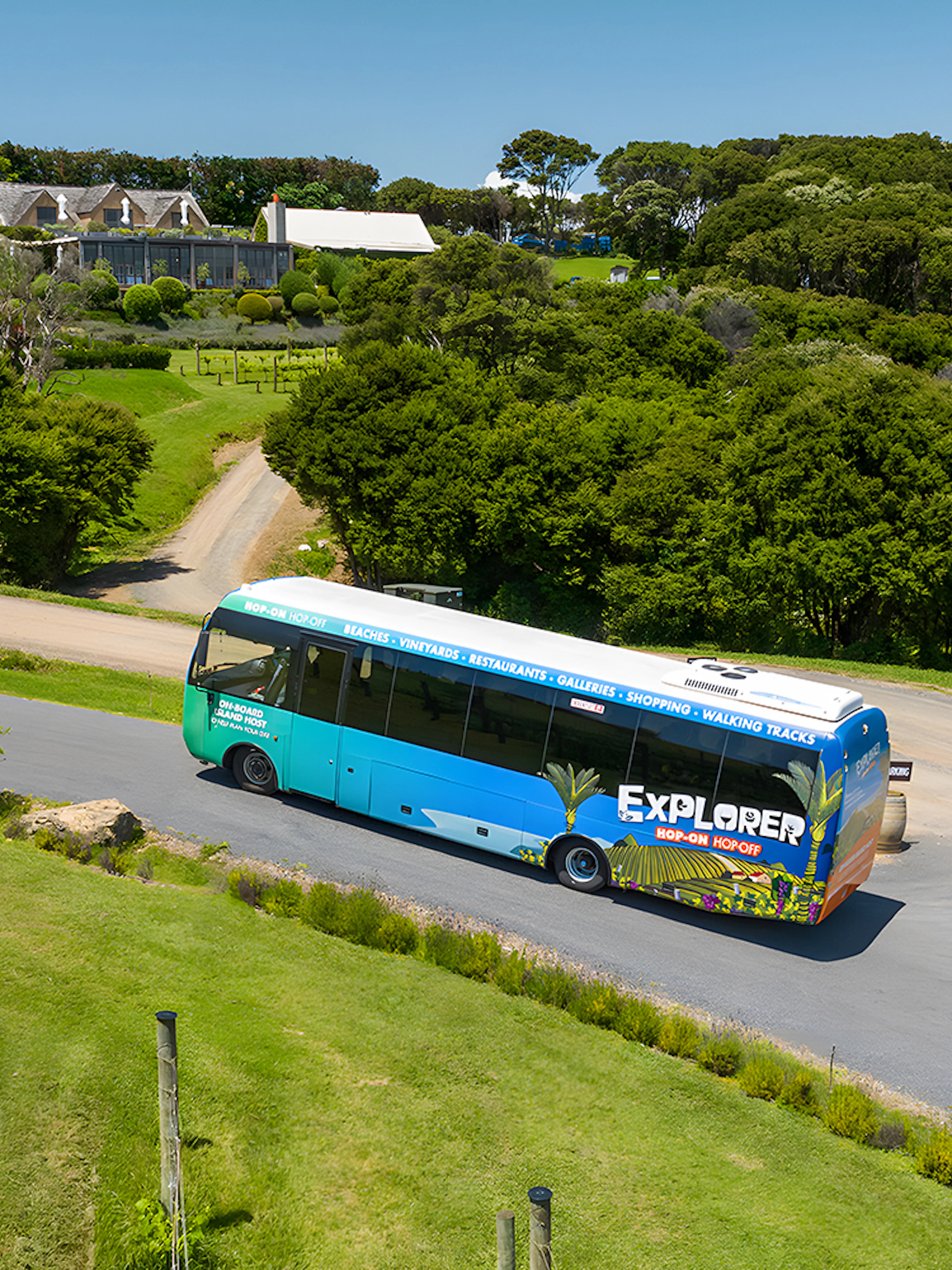 Hop-on hop-off bus touring Waiheke Island with lush greenery and a vineyard in the background.
