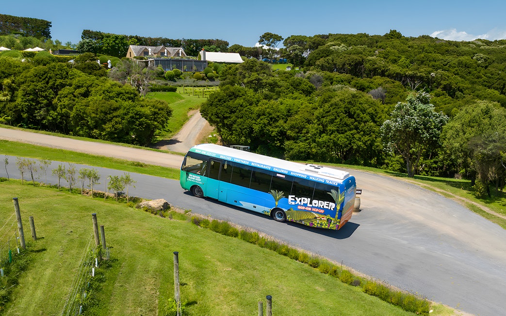 Hop-on hop-off bus touring Waiheke Island with lush greenery and a vineyard in the background.