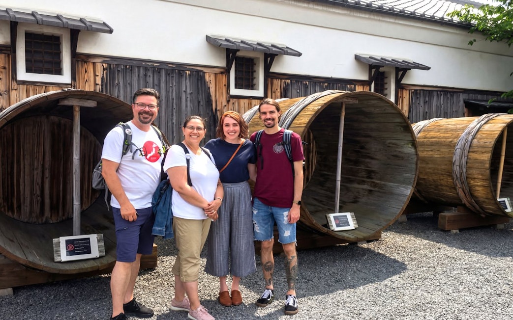 Group of tourists at a Kyoto sake brewery with large wooden barrels.