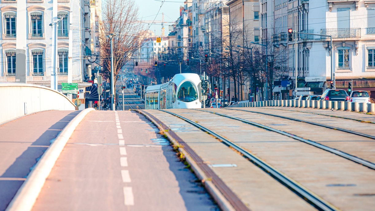 Tram crossing a bridge in Lyon, France, with city buildings in the background.